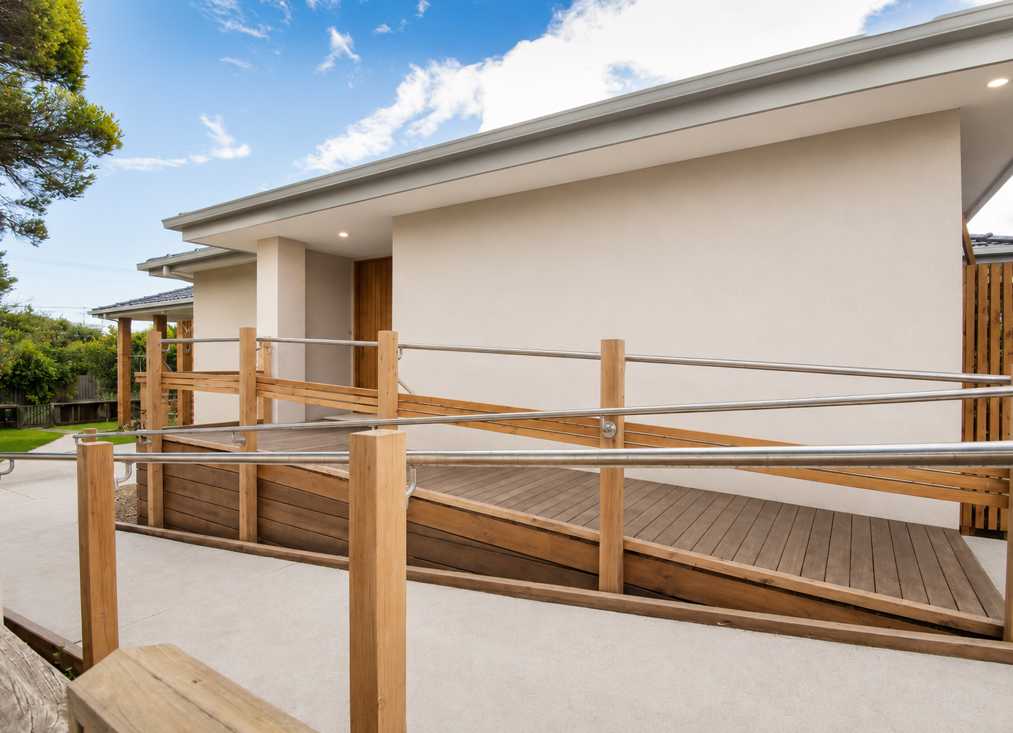 Accessible home entry with a timber and stainless-steel wheelchair ramp leading to a level, step-free doorway.