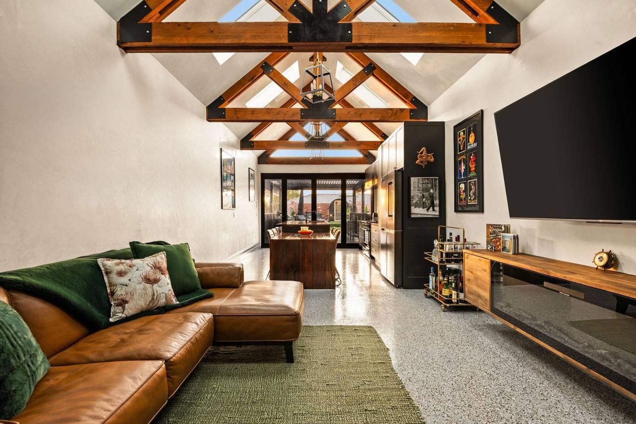 Open-plan living and kitchen area with a level polished-concrete floor, wide central walkway and a raked timber-truss ceiling.
